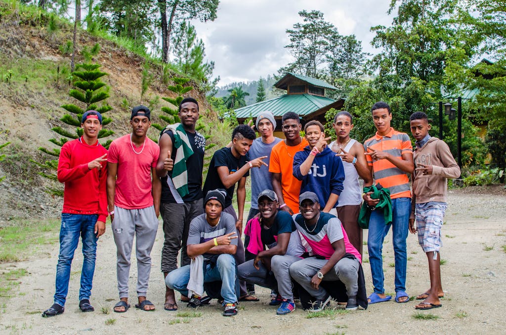 A group of young men poses outdoors with casual, colorful attire in a natural setting.