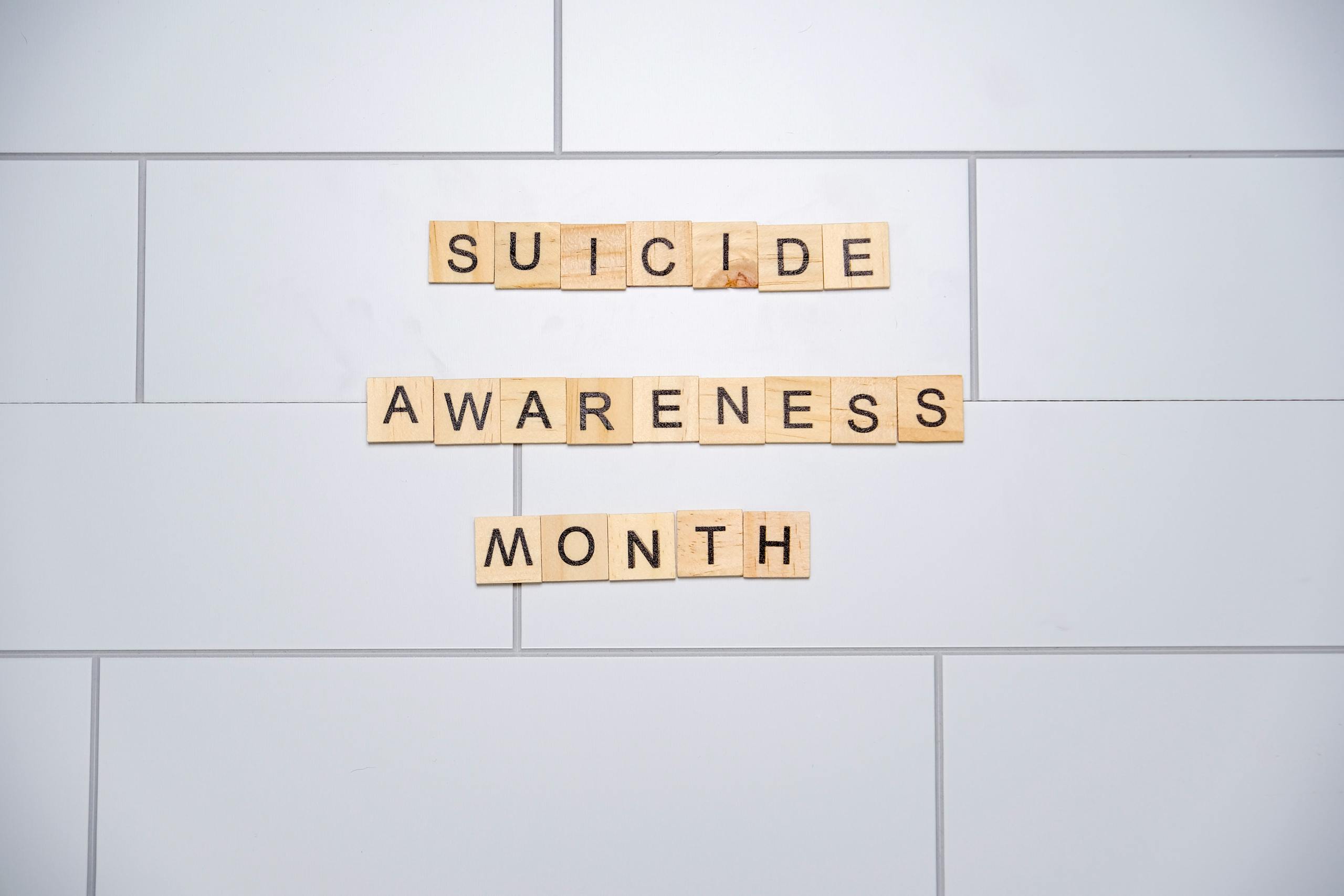 Wooden tiles spelling 'Suicide Awareness Month' on a white tiled background.